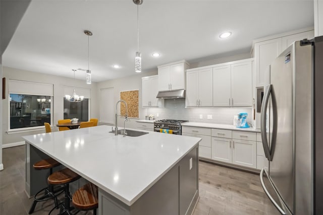 kitchen with a kitchen island with sink, sink, hanging light fixtures, and appliances with stainless steel finishes