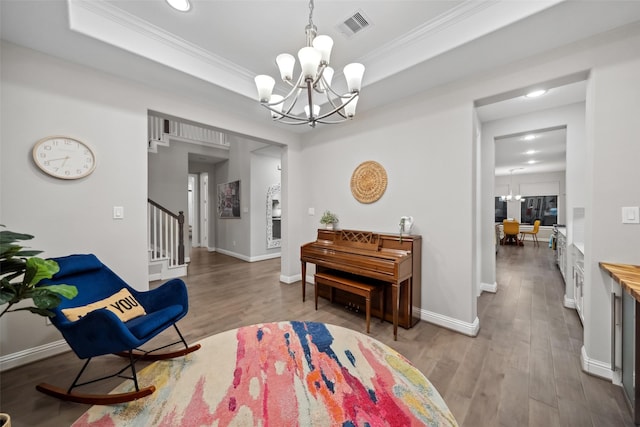 living area featuring a raised ceiling, light hardwood / wood-style flooring, an inviting chandelier, and ornamental molding