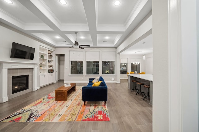 living room with hardwood / wood-style floors, coffered ceiling, ceiling fan with notable chandelier, a fireplace, and beam ceiling