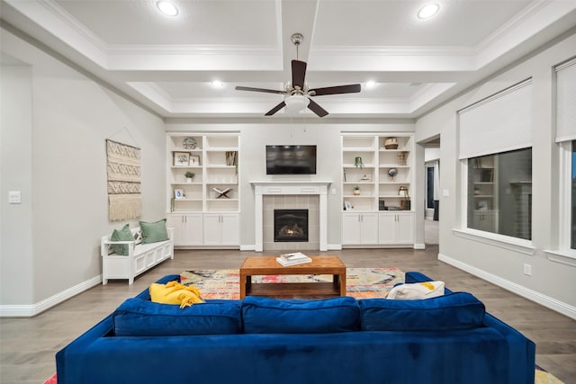 living room featuring crown molding, built in features, ceiling fan, a tiled fireplace, and hardwood / wood-style floors