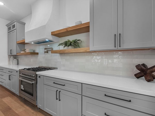 kitchen featuring tasteful backsplash, light hardwood / wood-style flooring, gray cabinets, stainless steel stove, and custom exhaust hood