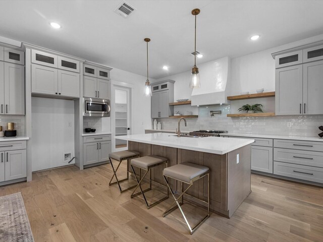 kitchen featuring premium range hood, a breakfast bar, decorative light fixtures, stainless steel microwave, and an island with sink