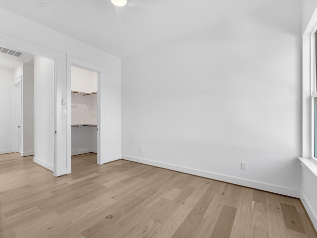 unfurnished bedroom featuring a walk in closet, light wood-type flooring, a closet, and ceiling fan