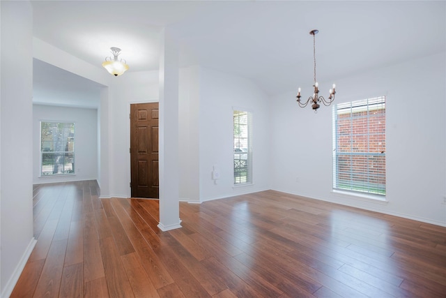 unfurnished room with vaulted ceiling, a wealth of natural light, dark wood-type flooring, and a notable chandelier