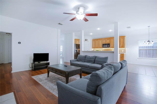 living room with ceiling fan with notable chandelier and dark wood-type flooring