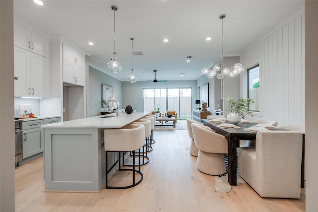 kitchen with a large island with sink, ceiling fan, light hardwood / wood-style flooring, and pendant lighting