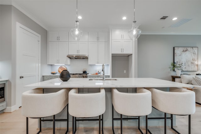 kitchen featuring white cabinetry, sink, crown molding, decorative light fixtures, and a center island with sink