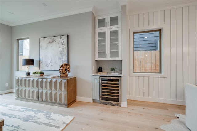 bar featuring wine cooler, light hardwood / wood-style flooring, decorative backsplash, ornamental molding, and white cabinetry