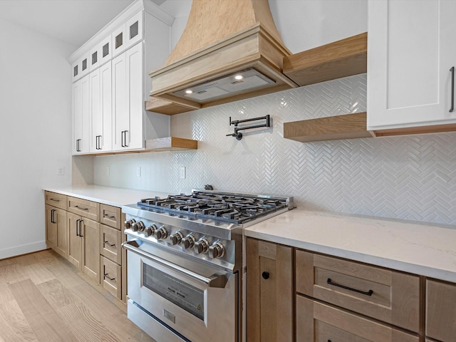 kitchen with backsplash, white cabinetry, light hardwood / wood-style floors, and high end stainless steel range oven