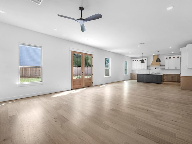 unfurnished living room featuring ceiling fan, a healthy amount of sunlight, french doors, and light hardwood / wood-style flooring