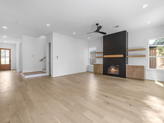 unfurnished living room featuring ceiling fan, a large fireplace, and light hardwood / wood-style flooring