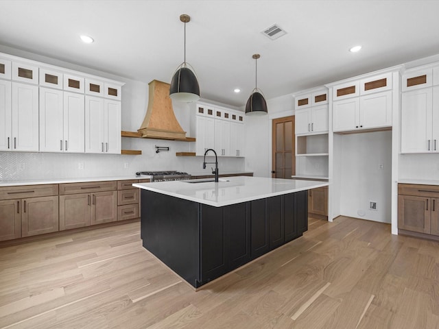 kitchen featuring white cabinets, premium range hood, and an island with sink