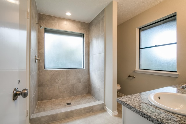 bathroom with a textured ceiling, vanity, tiled shower, tile patterned flooring, and toilet