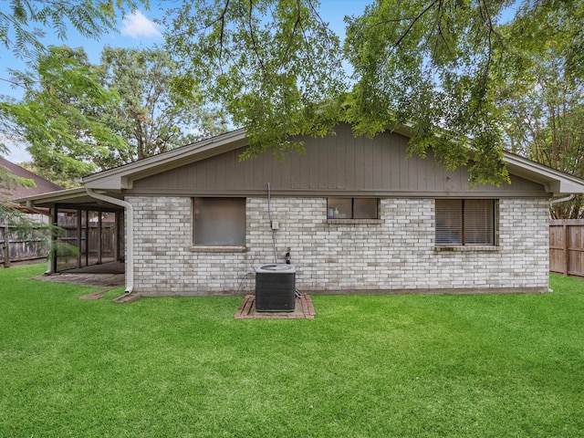 rear view of property with a sunroom, central AC unit, and a lawn