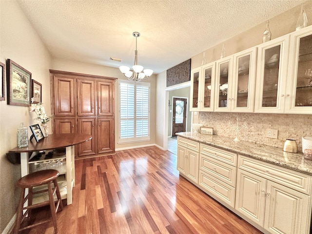 kitchen with backsplash, hanging light fixtures, light stone countertops, wood-type flooring, and a chandelier