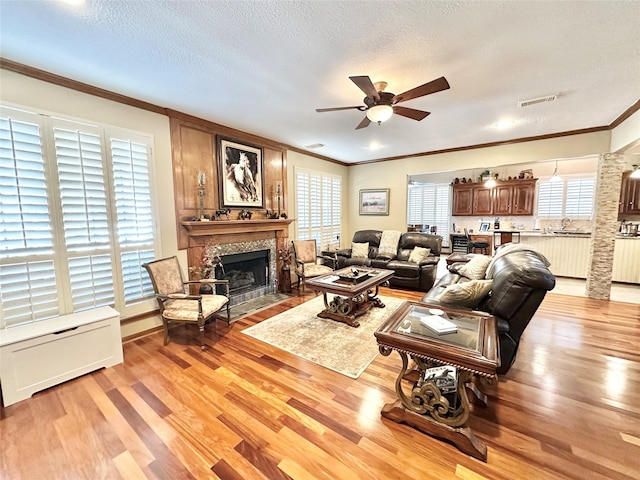 living room featuring ceiling fan, light hardwood / wood-style flooring, a textured ceiling, and ornamental molding