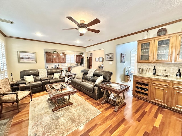 living room featuring bar area, ceiling fan, crown molding, and light wood-type flooring