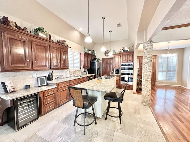 kitchen with appliances with stainless steel finishes, decorative columns, beverage cooler, sink, and an island with sink