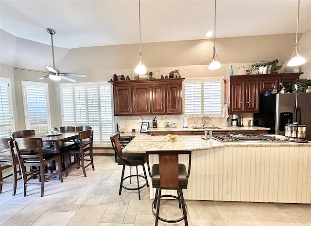 kitchen with decorative backsplash, light stone counters, stainless steel appliances, sink, and a breakfast bar area