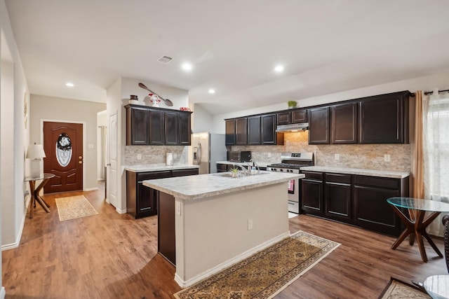 kitchen with decorative backsplash, stainless steel appliances, sink, a center island with sink, and light hardwood / wood-style flooring