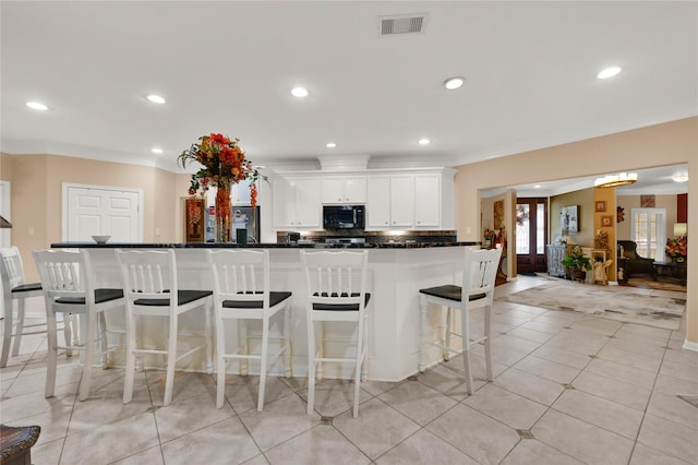 kitchen featuring a kitchen breakfast bar, white cabinets, tasteful backsplash, light tile patterned floors, and ornamental molding