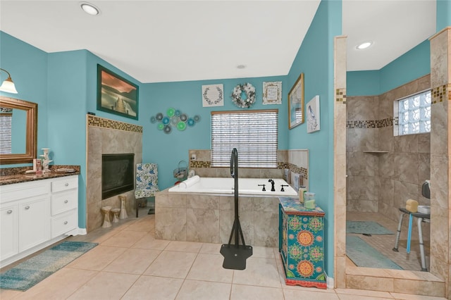 bathroom with plus walk in shower, a tile fireplace, vanity, and tile patterned flooring