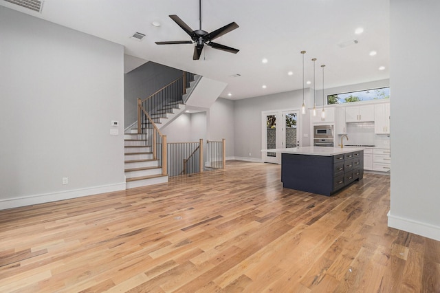 kitchen featuring light hardwood / wood-style flooring, decorative light fixtures, a kitchen island with sink, white cabinetry, and ceiling fan