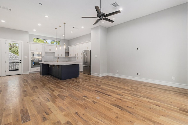 kitchen featuring white cabinetry, light hardwood / wood-style flooring, hanging light fixtures, a kitchen island with sink, and appliances with stainless steel finishes