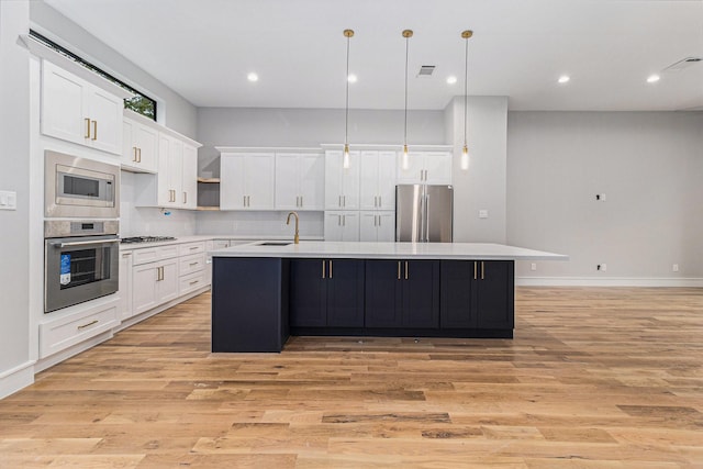 kitchen with stainless steel appliances, white cabinets, sink, and an island with sink