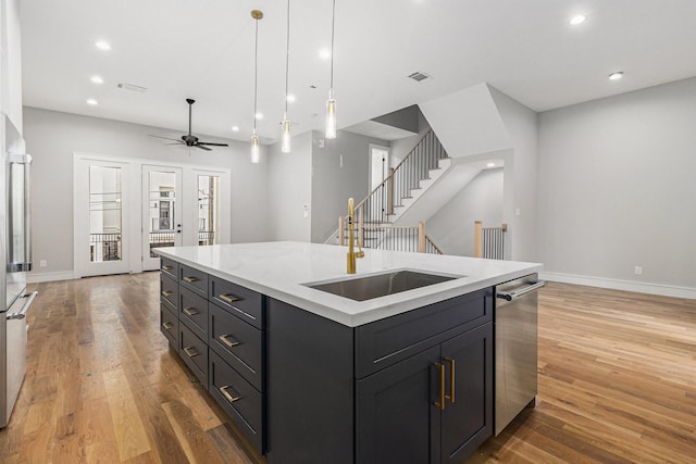 kitchen with hanging light fixtures, stainless steel appliances, a center island with sink, ceiling fan, and sink