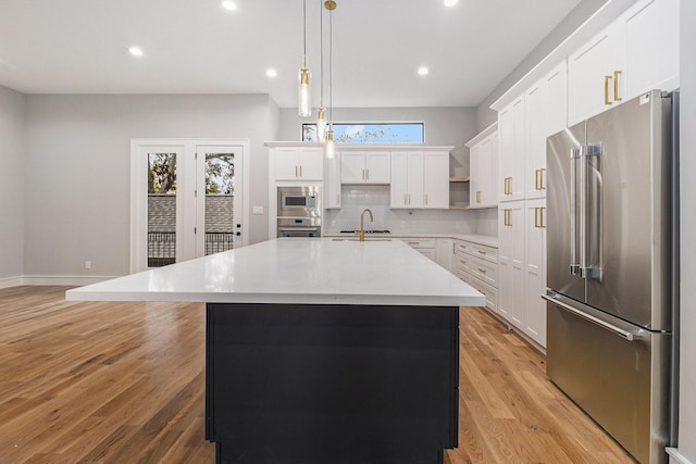 kitchen with stainless steel appliances, an island with sink, hanging light fixtures, white cabinetry, and tasteful backsplash