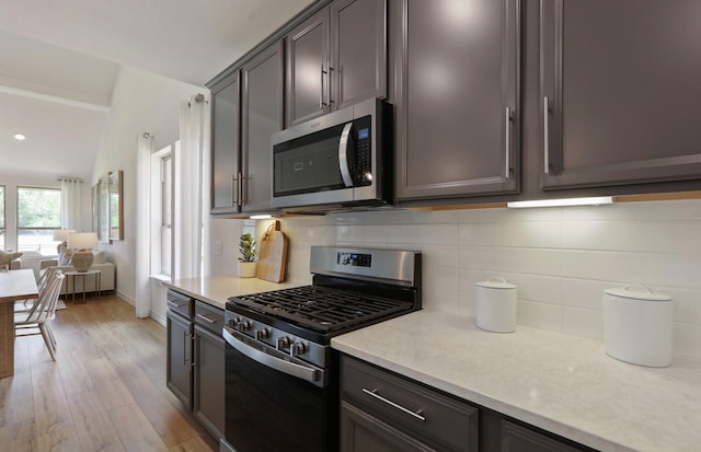 kitchen with backsplash, dark brown cabinetry, stainless steel appliances, and light hardwood / wood-style flooring