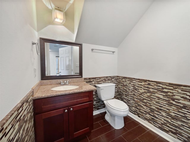 bathroom featuring vanity, toilet, lofted ceiling, and tile walls