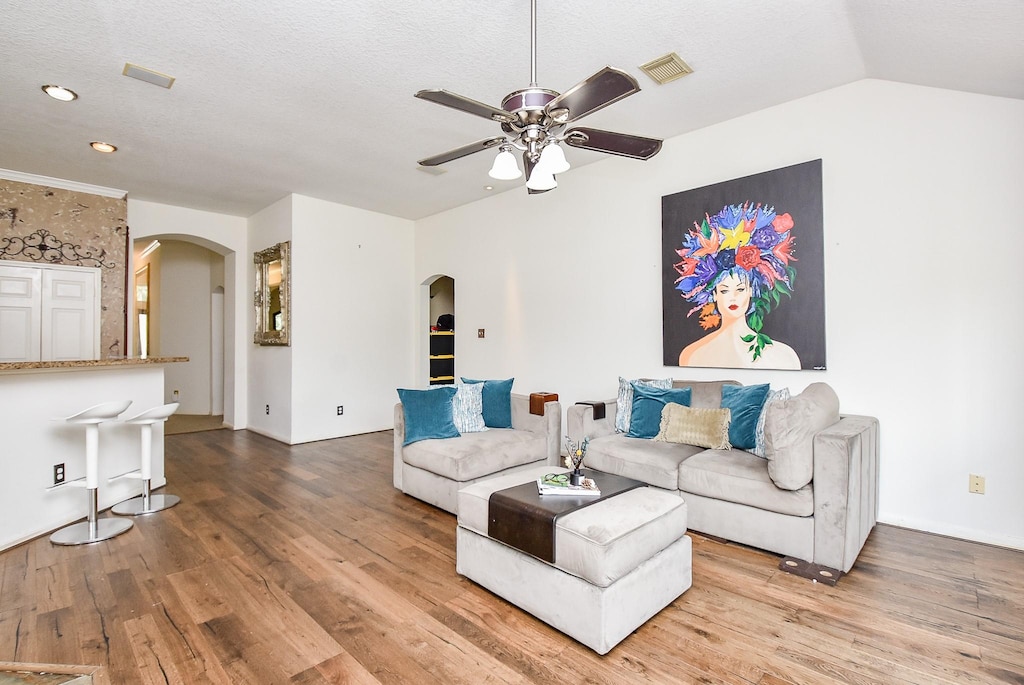 living room featuring wood-type flooring, a textured ceiling, vaulted ceiling, and ceiling fan