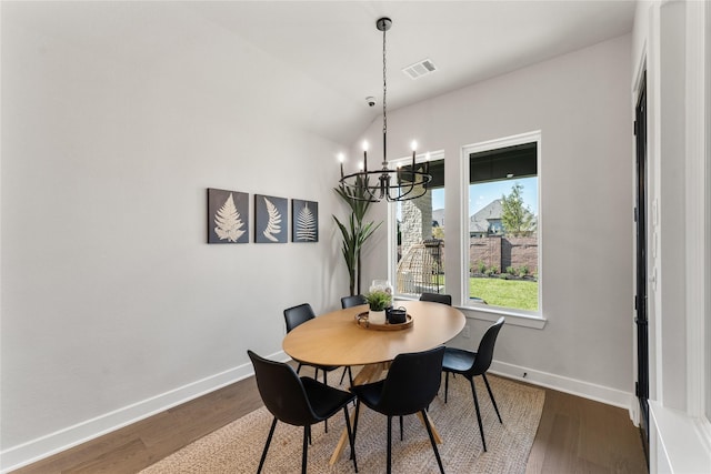 dining room with a notable chandelier, wood-type flooring, and vaulted ceiling