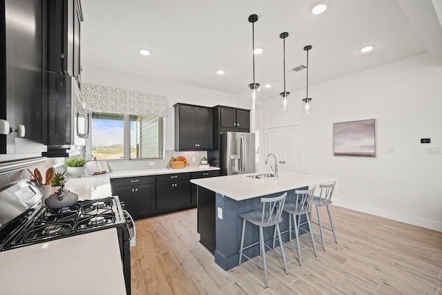 kitchen featuring a center island with sink, sink, hanging light fixtures, appliances with stainless steel finishes, and a breakfast bar area