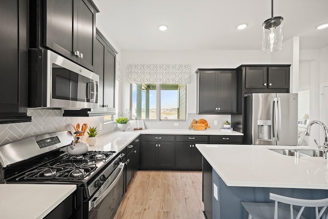 kitchen with sink, tasteful backsplash, light hardwood / wood-style floors, decorative light fixtures, and appliances with stainless steel finishes