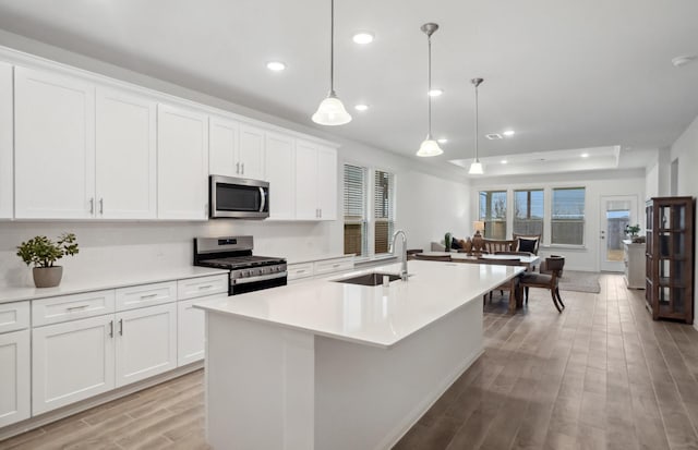 kitchen with appliances with stainless steel finishes, pendant lighting, an island with sink, sink, and white cabinets