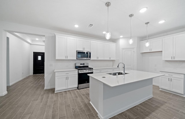 kitchen with appliances with stainless steel finishes, white cabinetry, sink, hanging light fixtures, and a center island with sink