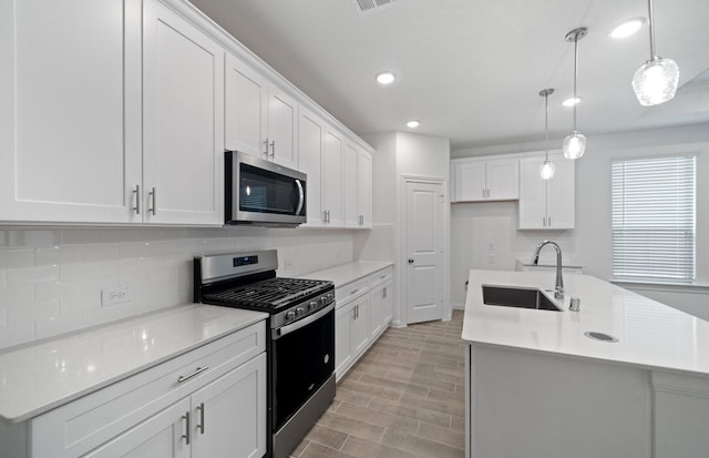 kitchen featuring appliances with stainless steel finishes, decorative light fixtures, sink, white cabinets, and a kitchen island with sink