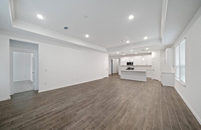 unfurnished living room with dark hardwood / wood-style floors, ornamental molding, and a tray ceiling