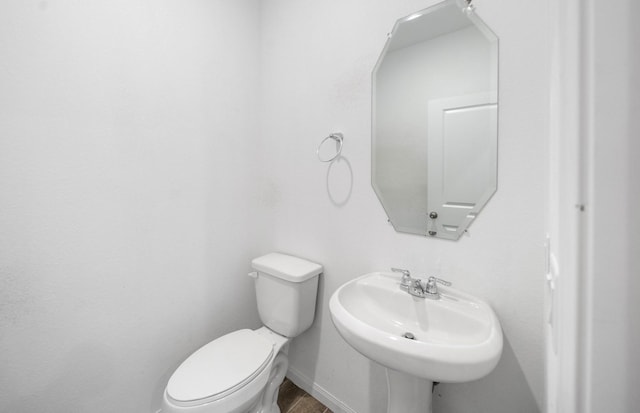 half bathroom featuring toilet, baseboards, and a sink