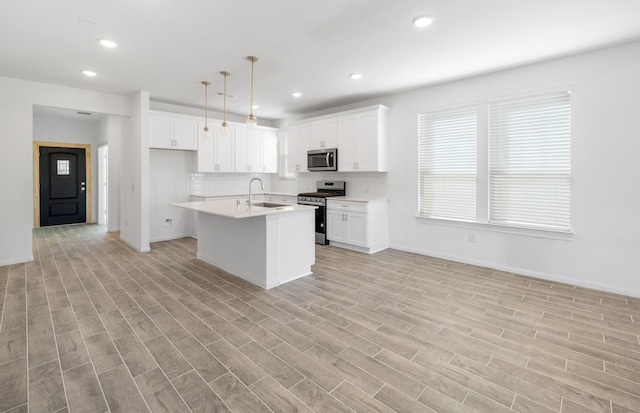 kitchen with stainless steel appliances, light countertops, hanging light fixtures, a kitchen island with sink, and a sink