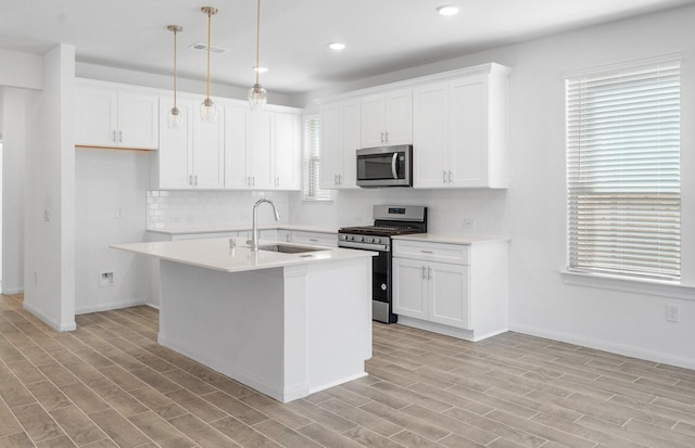 kitchen with decorative light fixtures, stainless steel appliances, a sink, light countertops, and a center island with sink