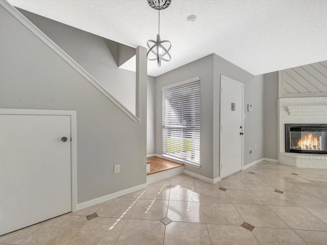 foyer entrance featuring a chandelier, light tile patterned flooring, a textured ceiling, and a brick fireplace