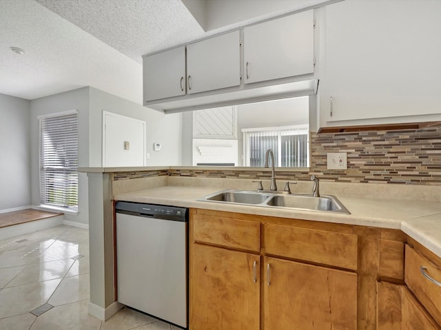 kitchen featuring sink, light tile patterned floors, stainless steel dishwasher, white cabinets, and backsplash