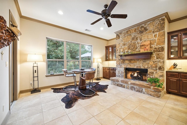 tiled living room featuring a stone fireplace, ceiling fan, and ornamental molding