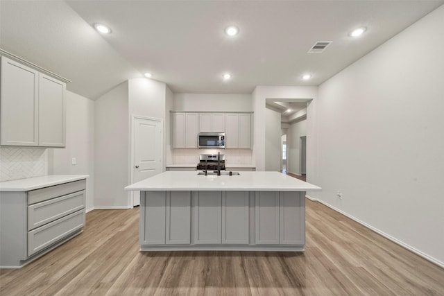 kitchen featuring sink, gray cabinets, light hardwood / wood-style floors, and a center island with sink