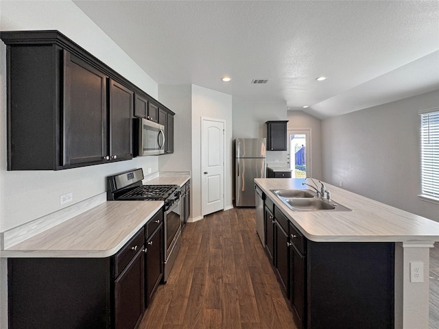 kitchen with sink, vaulted ceiling, an island with sink, appliances with stainless steel finishes, and dark hardwood / wood-style flooring