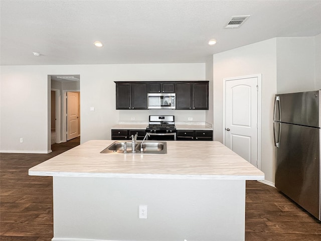 kitchen with sink, an island with sink, dark hardwood / wood-style floors, and appliances with stainless steel finishes